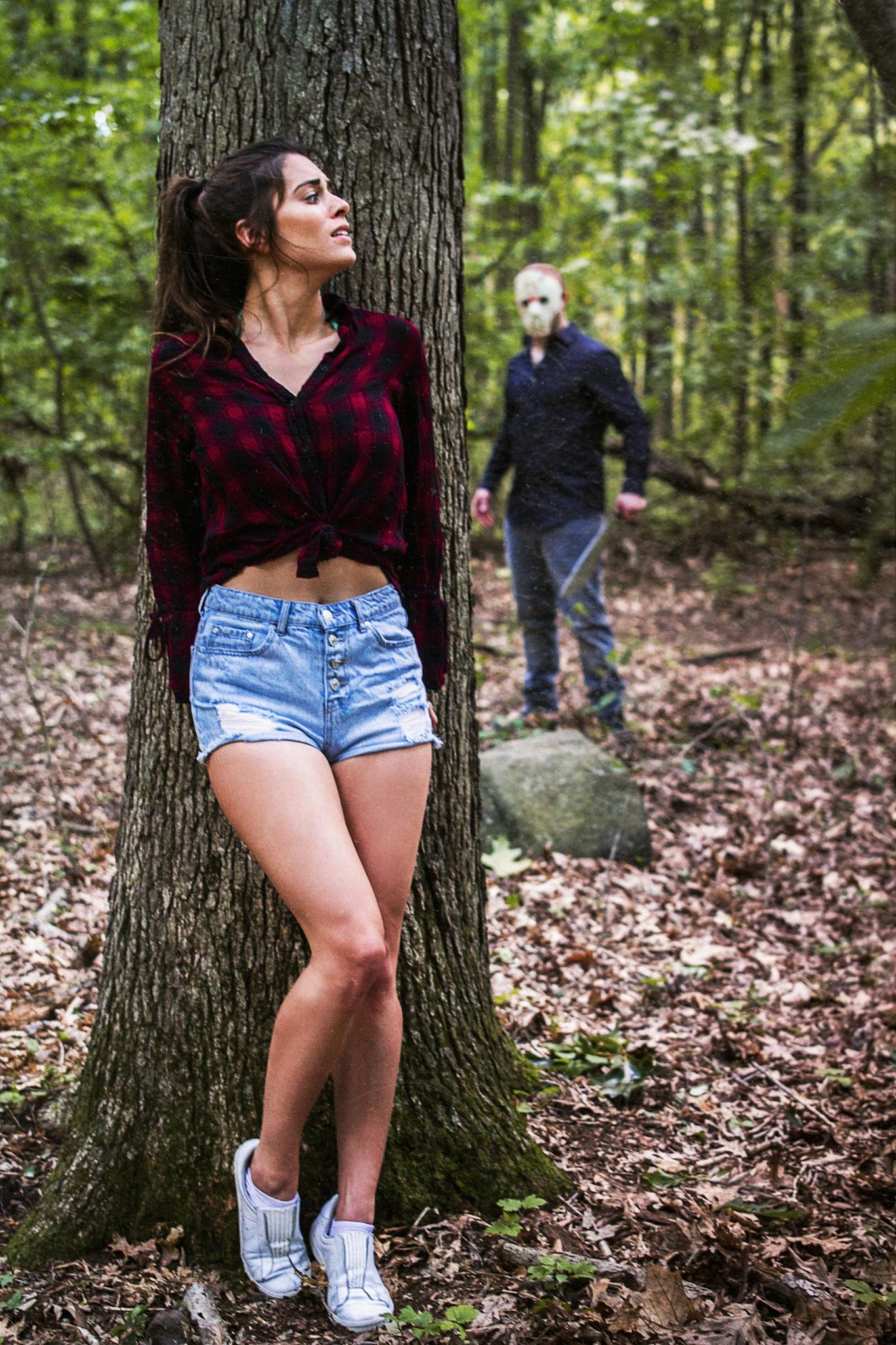 Cinematic horror scene with a woman in woods and masked figure, autumn setting.